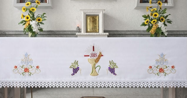 Mantel artesanal a medida con diseño religioso pintado a mano, decorado con flores, racimos de uvas y una cruz central. Confeccionado por Manos Maravillosas en Ibagué, Colombia.