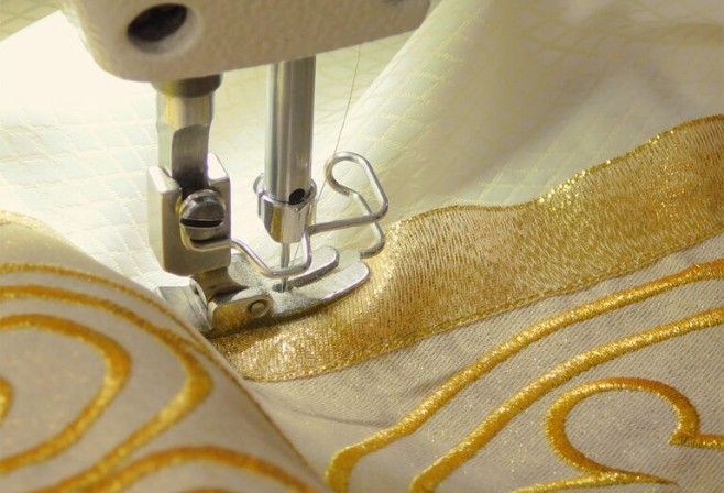Máquina de coser trabajando en un bordado dorado sobre tela litúrgica, muestra del trabajo artesanal y detallado de Manos Maravillosas en Ibagué, Colombia.